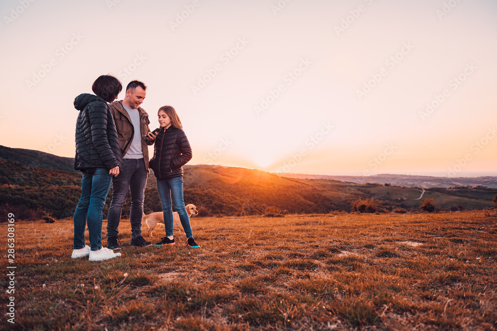 Family with dog standing on the hill and using smartphone
