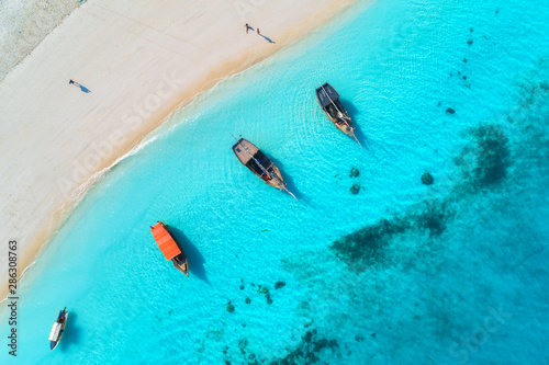 Aerial view of the fishing boats in clear blue water at sunset in summer. Top view from drone of boat, yacht, sandy beach. Indian ocean. Travel. Tropical seascape with sailboats, sea. View from above © den-belitsky