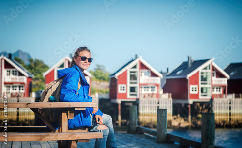 Beautiful young happy smiling girl traveler on the background of traditional red rorbu traveling to Lofoten Norway