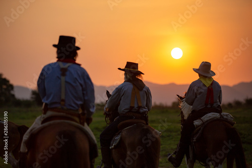 cowboy riding horse against sunset 