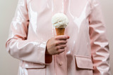 Close up of woman in pink raincoat holding vanilla ice cream in waffle cone. Minimalism concept.