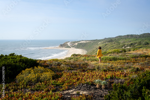 Girl view from the back and side standing on the grass with a view to the beach from the top of a mountain.