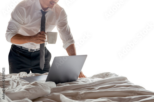 Businessman holding cup of coffee and working on laptop in bed room isolated. photo