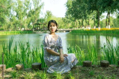 Beautiful woman sitting on the grass in the garden near lake