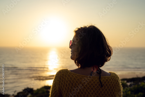 Woman with sunglasses watching the sunset on the beach below.