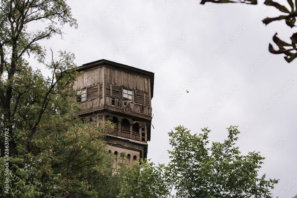 Abandoned tower in forest. Old wooden and brick building. Vintage architecture. Desolation concept. Retro house with wooden balcony. Facade of ruined high tower.