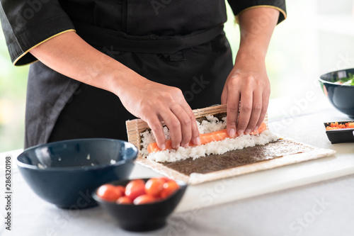 Chef preparing sushi. Asian woman chef in black uniform, about to roll salmon into sushi.