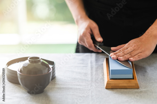 Chef sharpening knife on table. Japanese setting with asian woman. Light leaks effect.