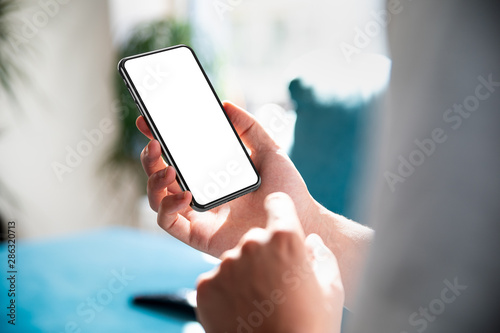 Man using smartphone blank screen frameless modern design while lying on the sofa in home interior photo