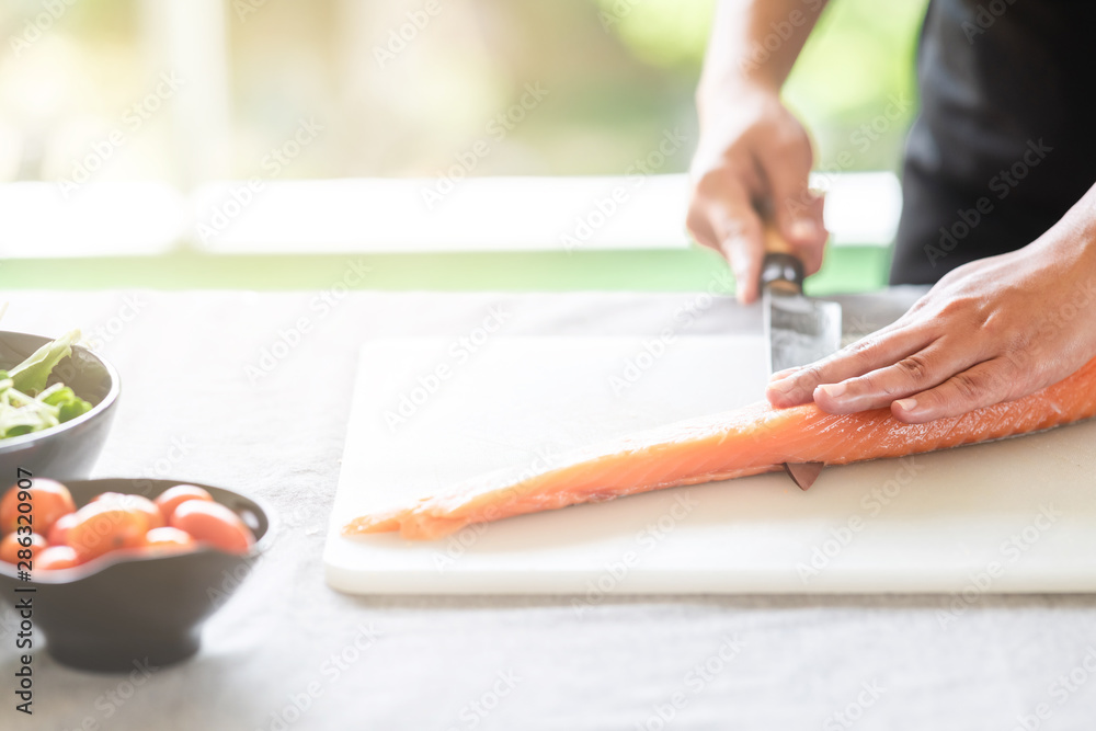Chef prepare to cut raw salmon. Asian woman chef in black uniform, slicing halfway of raw salmon with light leaks. Chef prepare to cut raw salmon. Asian woman chef in black uniform, slicing halfway of raw salmon with light leaks.
