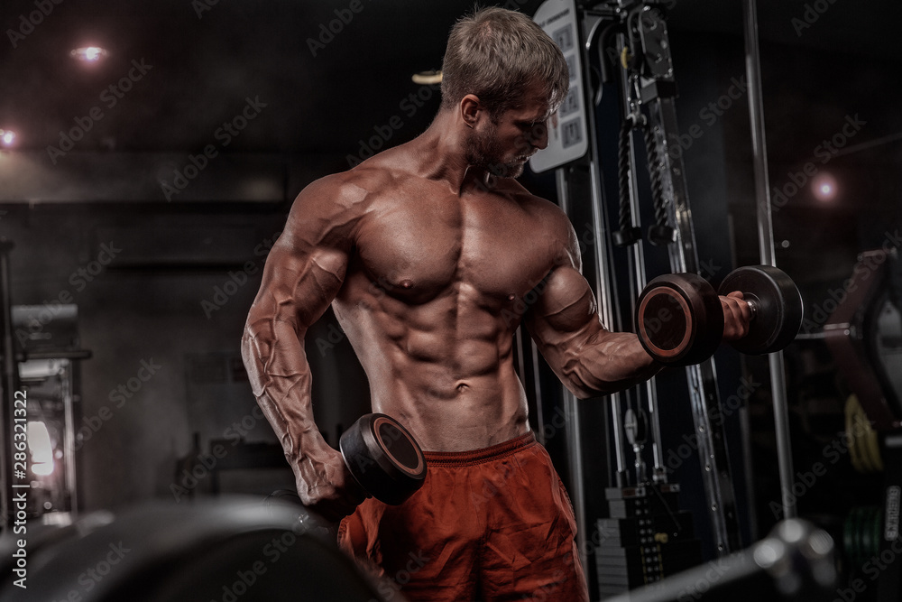 Brutal handsome Caucasian bodybuilder working out training in the gym gaining weight pumping up muscles and poses fitness and bodybuilding concept