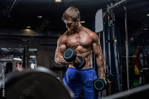 Attractive tall muscular bodybuilder doing heavy deadlifts in moder fitness center.