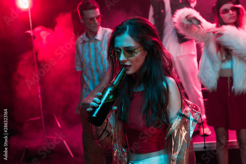 Photography beautiful girl in sunglasses drinking beer in nightclub during rave