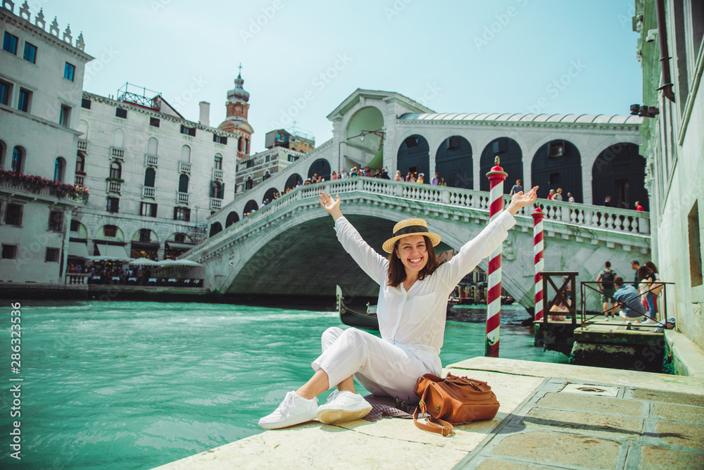 woman sitting near rialto bridge in venice italy looking at grand canal with gondolas - obrazy, fototapety, plakaty 