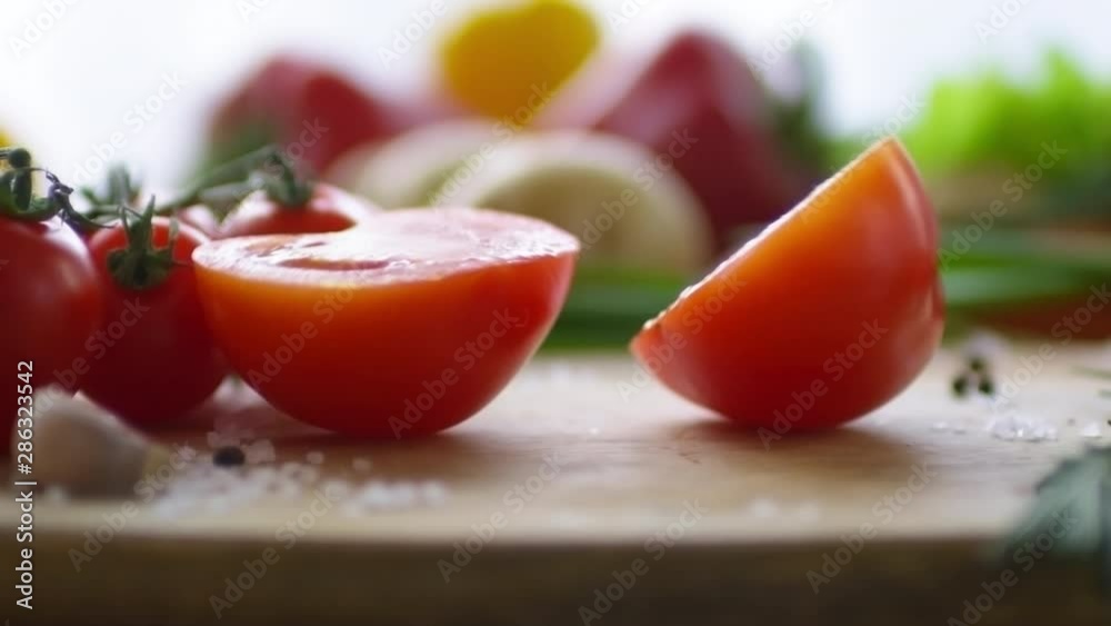 Close up view of fresh juicy tomato falling down on wooden cutting board and dividing into halves Close up view of fresh juicy tomato falling down on wooden cutting board and dividing into halves