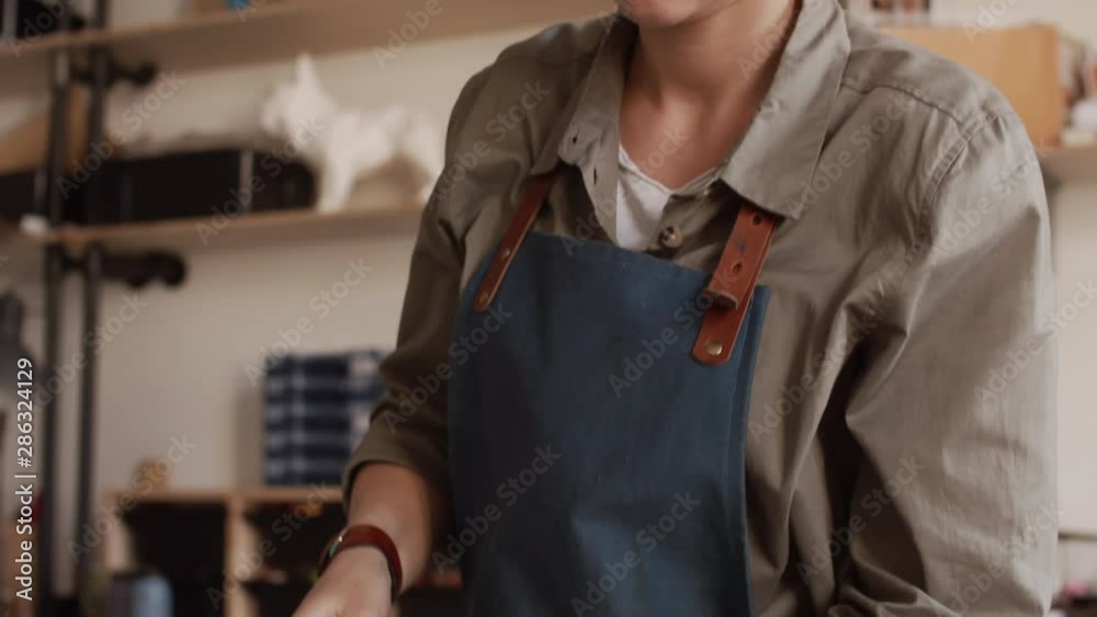 Tilt down of Caucasian craftswoman with blonde hair attaching leather strap to handmade leather bag in tannery Tilt down of Caucasian craftswoman with blonde hair attaching leather strap to handmade leather bag in tannery