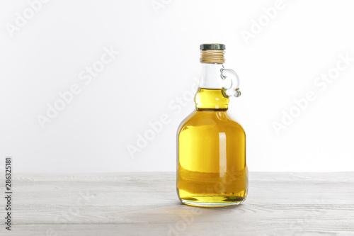 Transparent glass bottle of oil on white wooden table isolated on white
