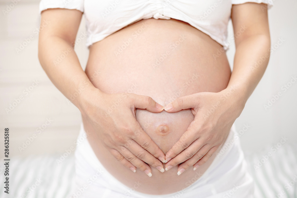 New mom Pregnant woman in white underwear Heart-shaped hand show love with baby. Young woman expecting a baby Stand in the outdoors. happy birthday