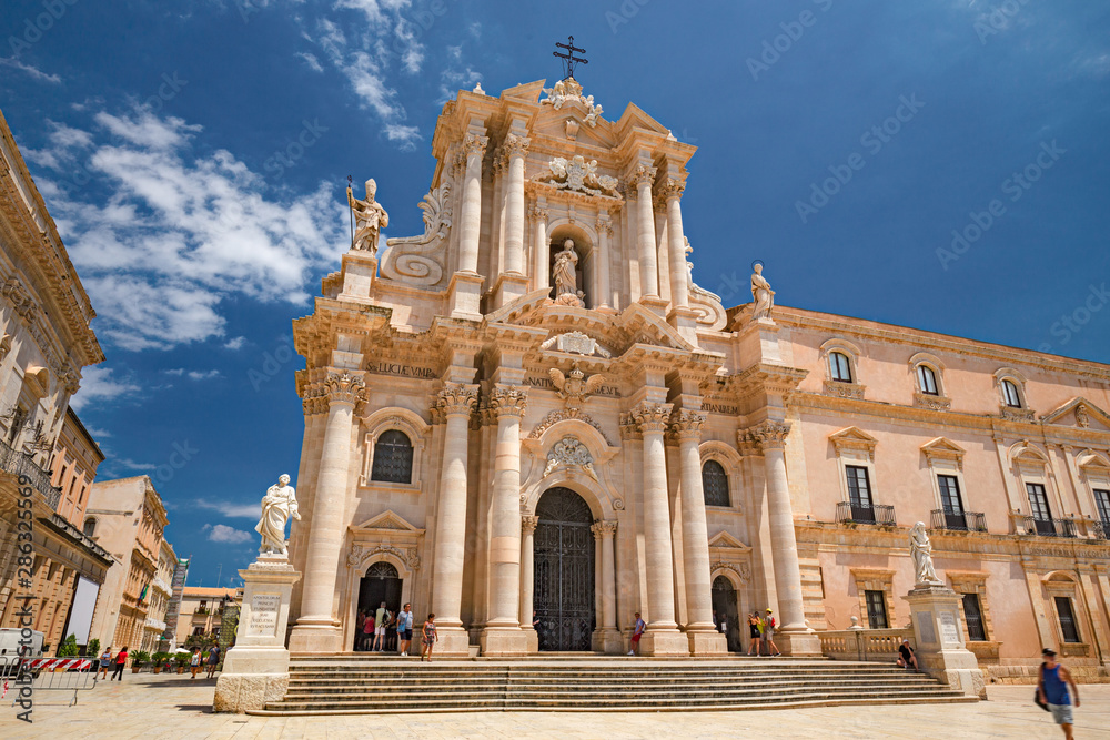 Some tourists are walking admiring the baroque cathedral in the historic center of the island of Ortigia in Syracuse, in Sicily, Italy.