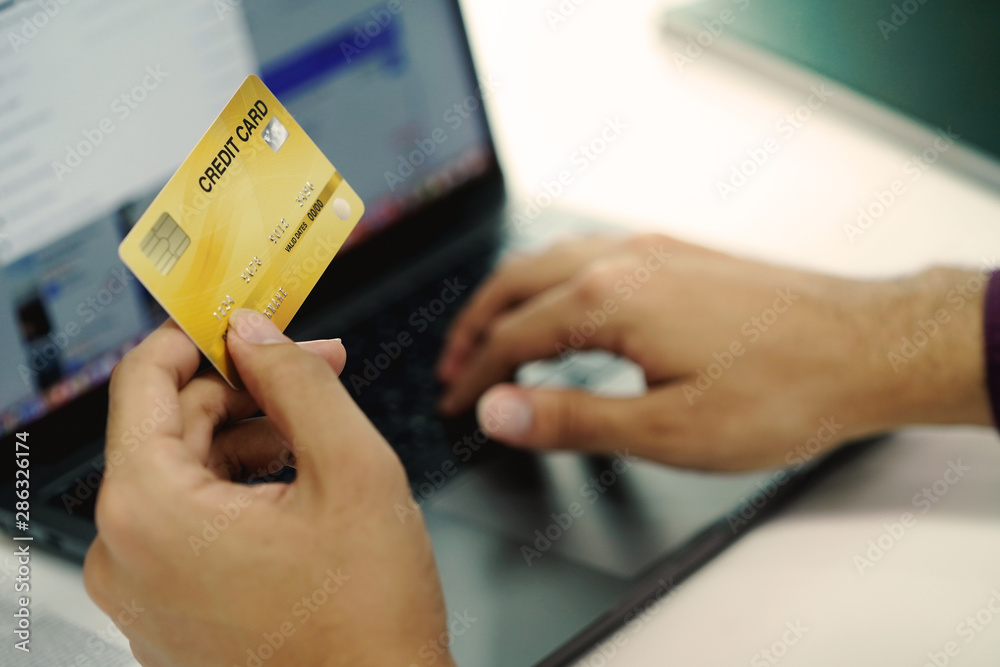Hand holding credit card, typing on the keyboard of laptop, online shopping and electronic payments concept. 