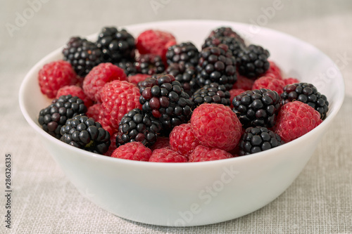Close ip of a white bowl with ruspberries and blackberries.