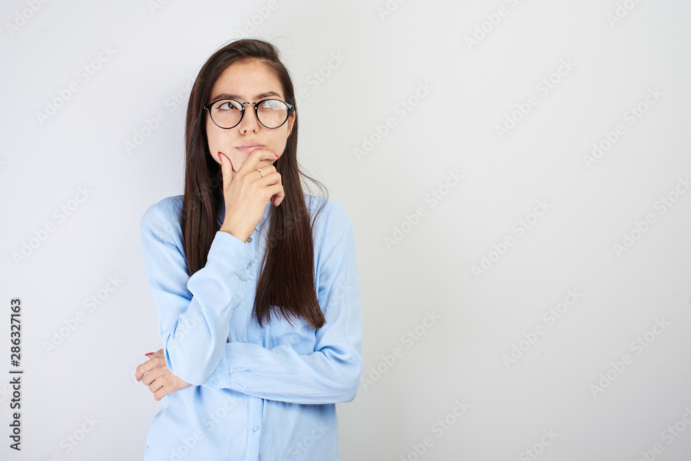 Portrait of Asian schoolgirl teenager Kazakh student in glasses with pensive face makes decision, thinking what choice to make, looks puzzled to the side on white background with blank copy space Portrait of Asian schoolgirl teenager Kazakh student in glasses with pensive face makes decision, thinking what choice to make, looks puzzled to the side on white background with blank copy space