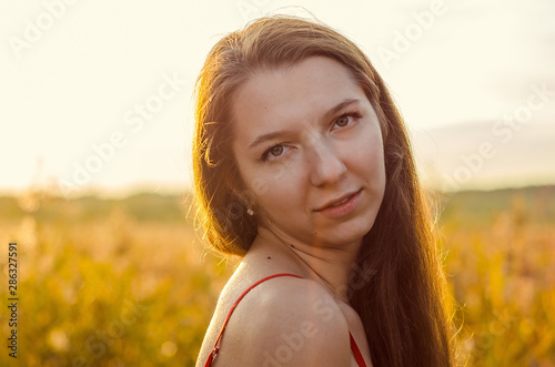 Beautiful girl in a posh red dress posing on a poppy field. Poppy field at sunset. Art processing. Sunset