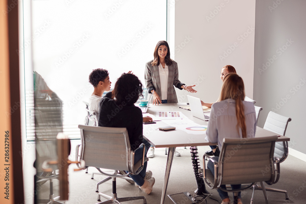 Female Boss Gives Presentation To Team Of Young Businesswomen Meeting Around Table In Modern Office - obrazy, fototapety, plakaty 