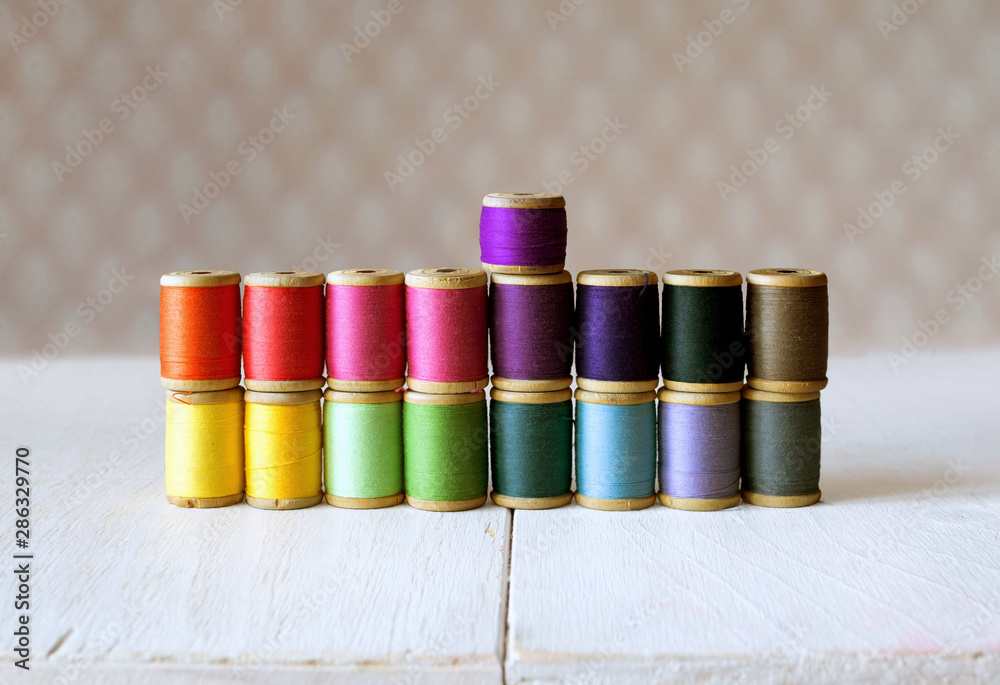 Multicolor rainbow old spools of sewing threads set on table, sewing supplies Multicolor rainbow old spools of sewing threads set on table, sewing supplies