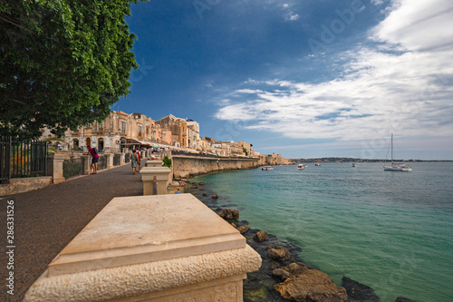 Some tourists walking along the seafront in the historic center of the island of Ortigia in Syracuse, Sicily Italy.