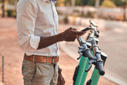 Young african guy is paying for electrical scooter by web payment using his mobile phone.