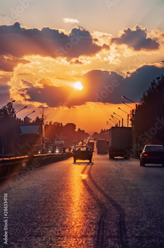 Highway with cars traveling on the sunset. Horizon line with the sun and storm clouds. Journeys. Selective focus.