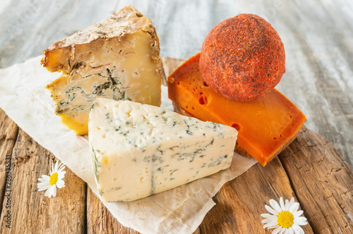 Delicatessen spicy cheeses of different varieties. Red cheddar, Dor blue, Stilton, Belper knoll on a beautiful textured wooden background. Spicy appetizer for gourmets. Selective focus photo