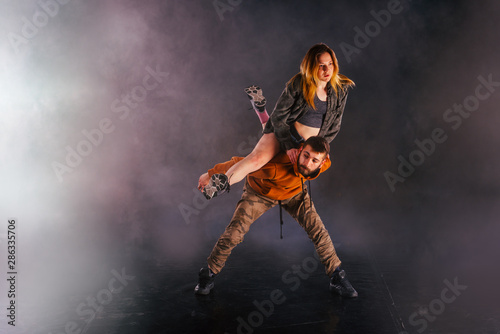 Strong male dancer and an elegant female dancer perform an exotic and unique dance moves in front of a black background while wearing urban clothes.