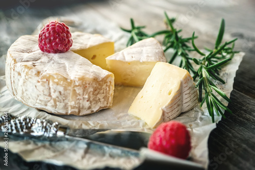 Delicatessen spicy Camembert cheese, brie with rosemary and raspberry on a beautiful textured wooden background. Spicy appetizer for gourmets. Selective focus