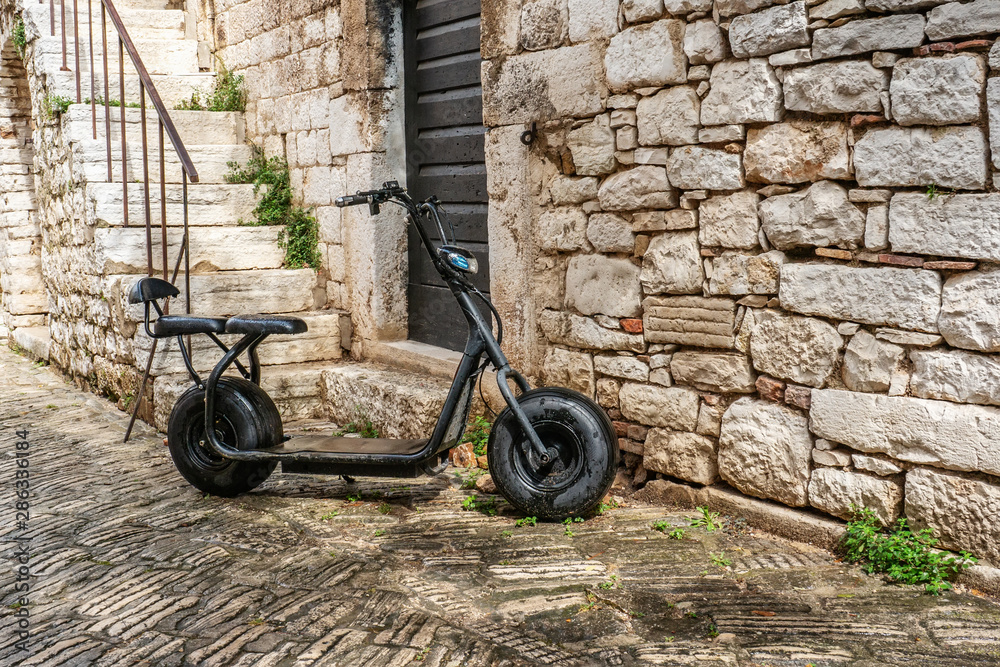 Fototapeta premium An old black Scooter is parked on the street by the stone wall. Urban eco-friendly transport