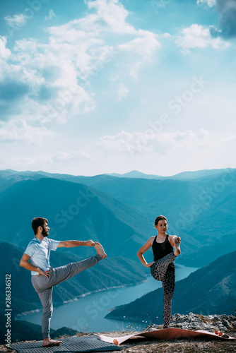 Two people is practicing yoga in high mountains