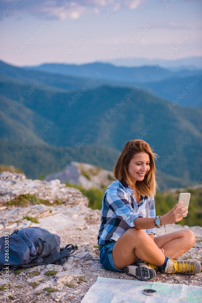 Young lady taking selfie with her phone while marveling the view from the top of the world at sunset. Success, winner, zen, tranquility.