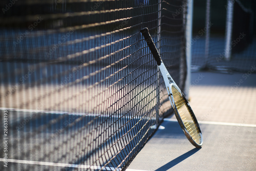 Tennis racquet is standing near tennis net outside at bright sunny day. Tennis racquet is standing near tennis net outside at bright sunny day.