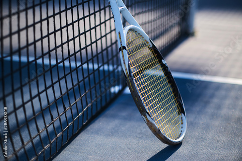 Tennis racquet is standing near tennis net outside at bright sunny day.
