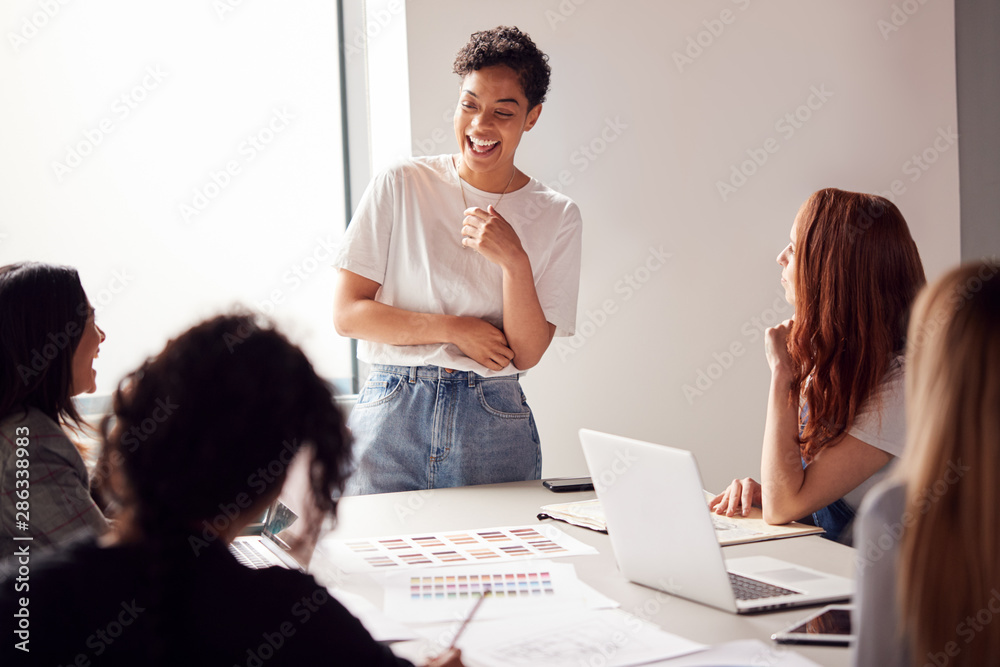 Female Boss Gives Presentation To Team Of Young Businesswomen Meeting Around Table In Modern Office