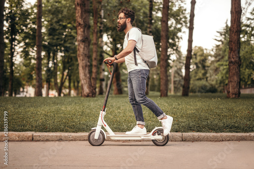 Modern citizen traveling by eco electric scooter on sidewalk