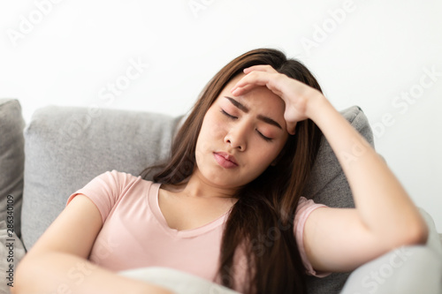 Asian young woman holding her hands on the forehead and have a headache on the sofa.
