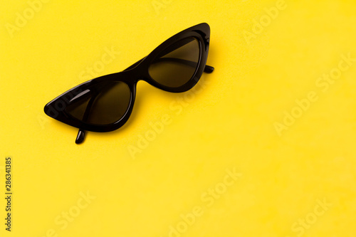 Black modern fashionable sunglasses on yellow background.