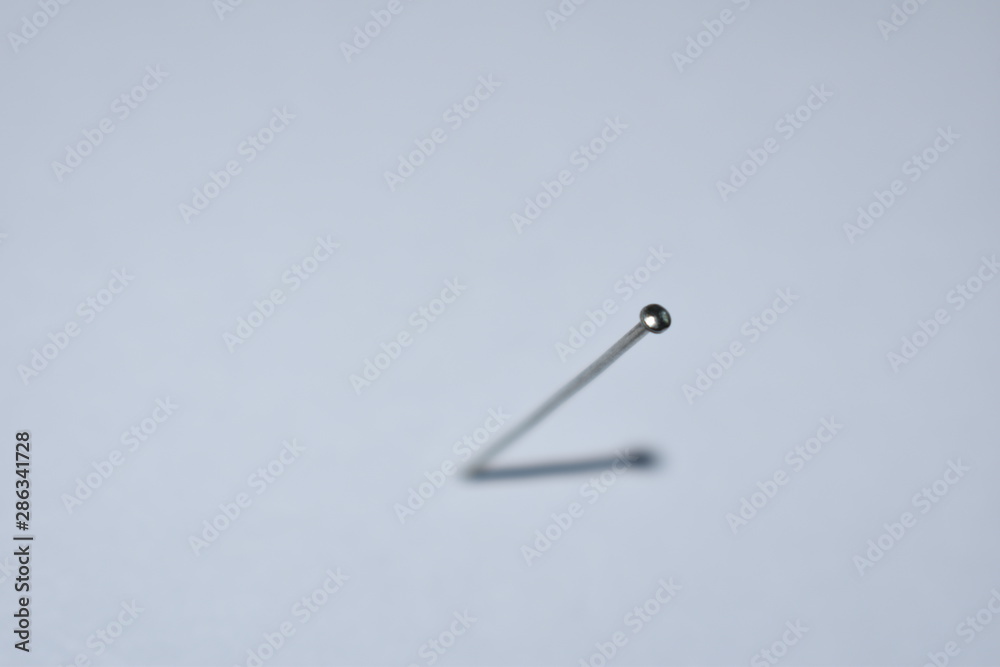 A nail on a light background with its shadow depicts a clock hand A nail on a light background with its shadow depicts a clock hand