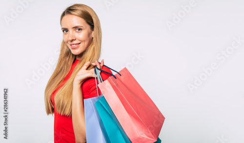 Beautiful young happy trendy blonde woman with colorful shopping bags in hands is posing in studio and looks on camera