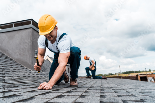 selective focus of handyman holding hammer while repairing roof near coworker