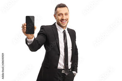Young man in a suit showing a mobile phone and smiling