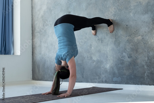 Woman learning to stand on hands near wall. Upside down yoga position. Studio shot