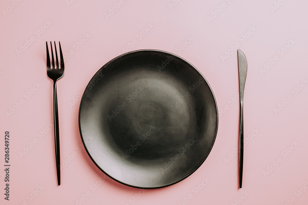 Black setting: plates, inen napkin and silverware on pink background. Top view. Black setting: plates, inen napkin and silverware on pink background. Top view.
